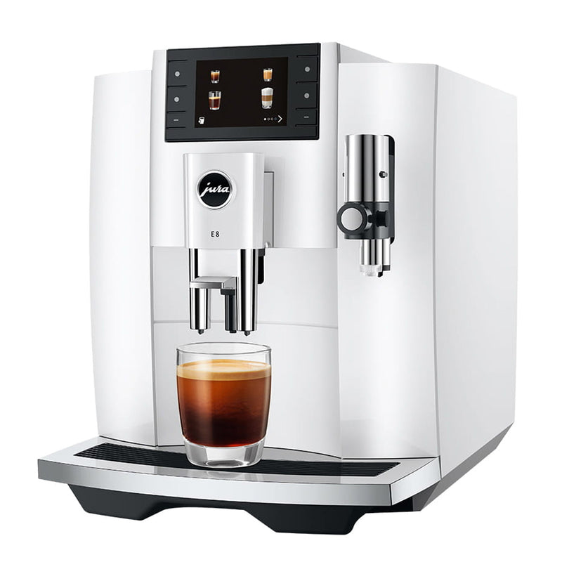 A modern, white Jura E8 Piano White Automatic Coffee Machine 15683 (Latest Version) with a digital display showing beverage options. A freshly brewed barista-quality coffee is placed under the dual spout on the tray. The machine, featuring advanced brewing technology, includes a milk frother on the right side.