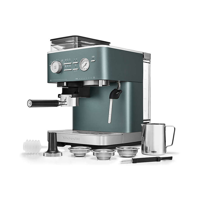 A KitchenAid Semi Automatic Espresso Machine with Burr Grinder KES6551JP (Juniper) featuring Smart Dosing Technology and various accessories, including portafilters, a milk frothing pitcher, a tamper, and cleaning tools. Displayed on a white background, the machine features knobs, buttons, and a built-in steam wand for precise brewing.