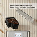 A removable bean hopper filled with coffee beans is detached from the KitchenAid KF8 Fully Automatic Espresso Machine (Brushed Stainless Steel) KES8558SX. A transparent lid is shown above the hopper. The background features a beige marble wall. The text on the image reads: "Easily change, exchange or refill beans in the removable bean hopper.