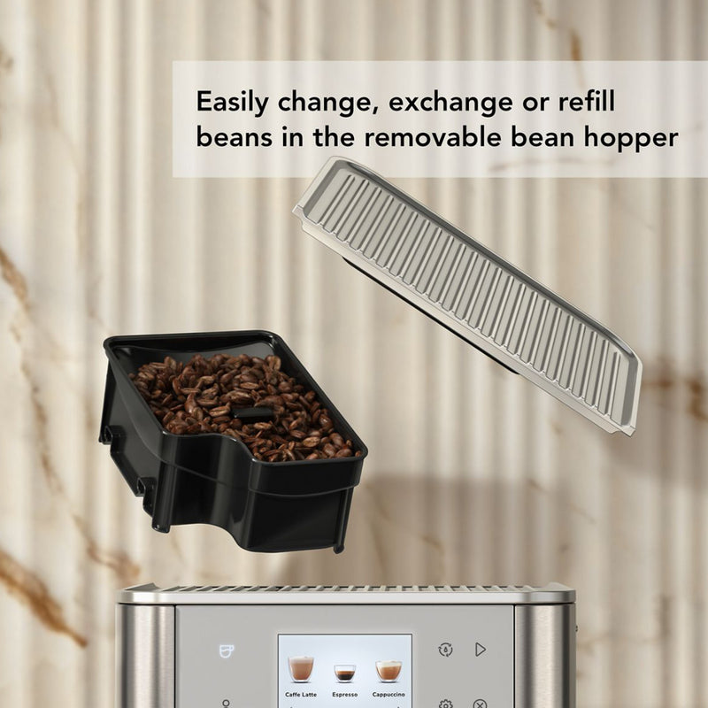 A removable bean hopper filled with coffee beans is detached from the KitchenAid KF8 Fully Automatic Espresso Machine (Brushed Stainless Steel) KES8558SX. A transparent lid is shown above the hopper. The background features a beige marble wall. The text on the image reads: "Easily change, exchange or refill beans in the removable bean hopper.