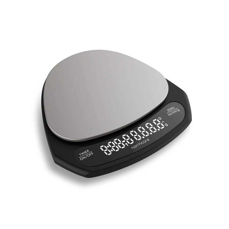 The Normcore Ultra Thin Coffee Scale by Normcore features an ultra-thin design with a round, metallic weighing surface. Its black base includes a digital screen that displays numbers and has buttons labeled "TARE," "ON/OFF," and "UNITS." With high precision weighing accuracy and a USB-C rechargeable battery, it is perfect for coffee enthusiasts.