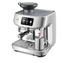 The Breville Oracle Jet Espresso Machine BES985BSS, crafted from brushed stainless steel, boasts a built-in grinder along with a digital display. It features two spouts and includes a steam wand for frothing milk in a stainless steel pitcher. The prominent "Breville" logo on the front assures users of commercial-grade performance coupled with advanced automation.