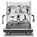 The ECM Synchronika II Espresso Machine, a stainless steel dual boiler with PID, features two pressure gauges, a central portafilter, steam wands on either side, control buttons at the bottom, rapid heat-up tech, and a "Caution: Hot Surface" label on top. Now available for preorder by ECM.