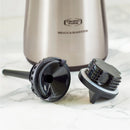 A close-up image of two coffee brewing accessories placed on a marble countertop, with part of a polished silver Technivorm Moccamaster KBT Thermal Carafe Brewer 79112 by Moccamaster visible in the background. Both sleek black accessories, designed for various brewing functionalities, feature durable borosilicate glass linings.