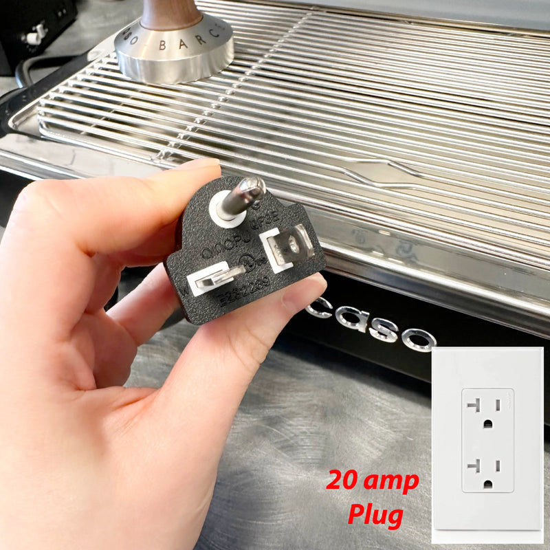 A hand is holding a 20 amp plug in front of an Ascaso Baby T Plus Espresso Machine BT203U (Black) with a metallic surface. In the bottom right corner, there is an image of a 20 amp outlet with the label "20 amp Plug" in red text.