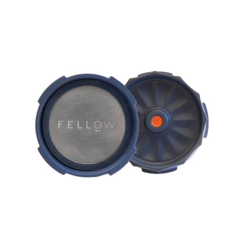 Two blue, round coffee accessories for your AeroPress Coffee Maker. One is the Fellow mesh coffee filter with "FELLOW" branded on it, and the other, shown from the side, features a raised orange center and appears to be a twist-on cap or lid—a perfect setup for espresso-style coffee using the Fellow Prismo Aeropress Coffee Maker Attachment.