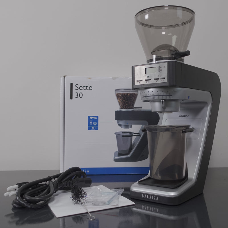 Image of a Baratza Sette 30 AP (All Purpose) Conical Burr Coffee Grinder - Open Box (2562) in front of its packaging box. Perfect for any espresso journey, the grinder is equipped with a digital display, hopper, and grounds container. Also included are a cleaning brush, power cord, manual, and spare parts. The box features an image of the conical burr grinder from Baratza.