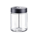 A transparent cylindrical Miele Glass Milk Container with a capacity of 0.7L features a black lid. Inside the jar, a metal rod extends from the lid to the base, indicating it could be an accessory for a Miele coffee machine or serve as a storage jar with a sealing mechanism. The empty container is set against a white background.
